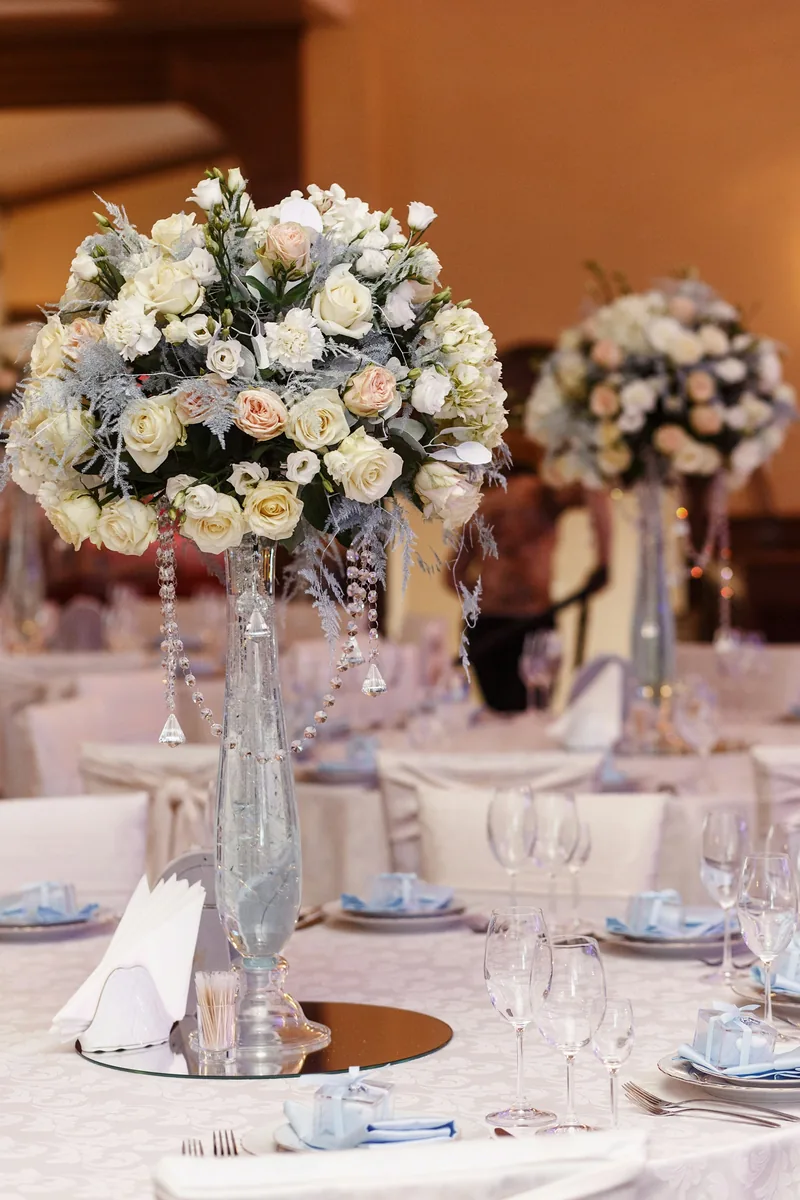 Tall white and blush floral centerpieces on formally set reception tables in a ballroom