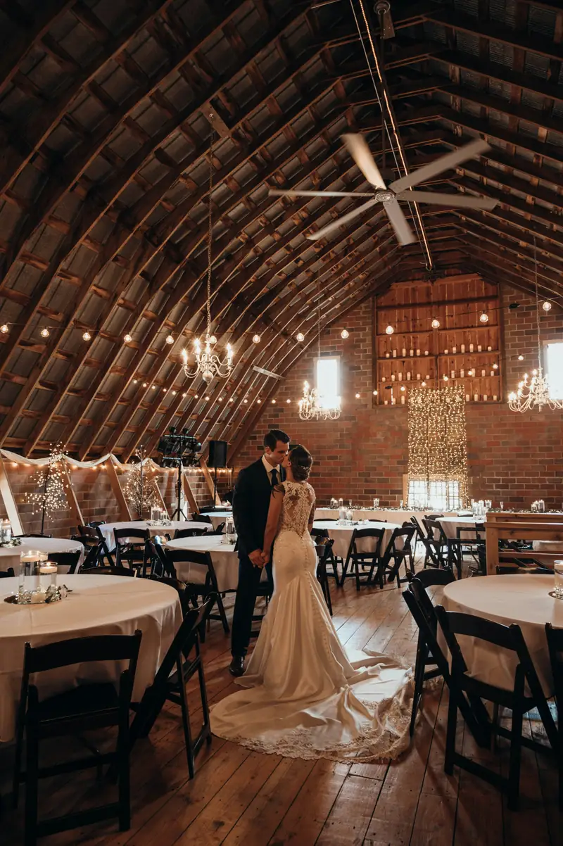 A couple dancing alone in a barn hung with chandeliers and string lights