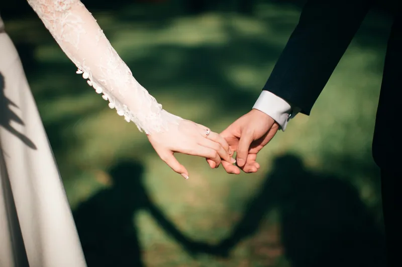 A bride and groom holding hands outdoors, her engagement ring catching the light