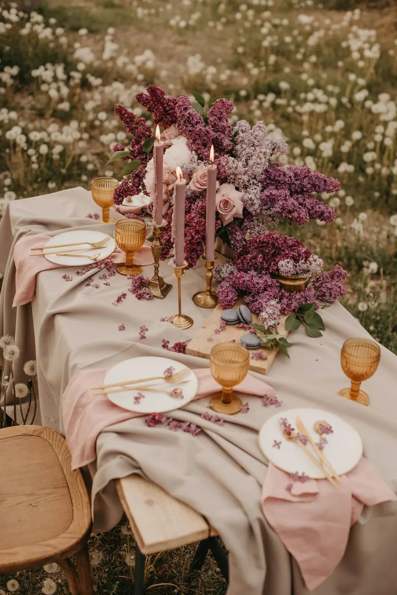 An intimate table set with lilacs and taper candles in an open meadow