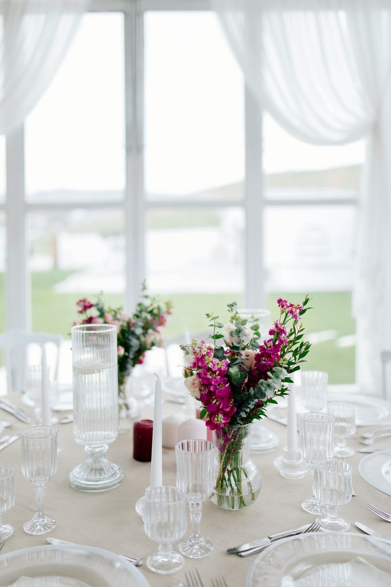 Reception tables in a white draped marquee with tall windows looking onto a lawn