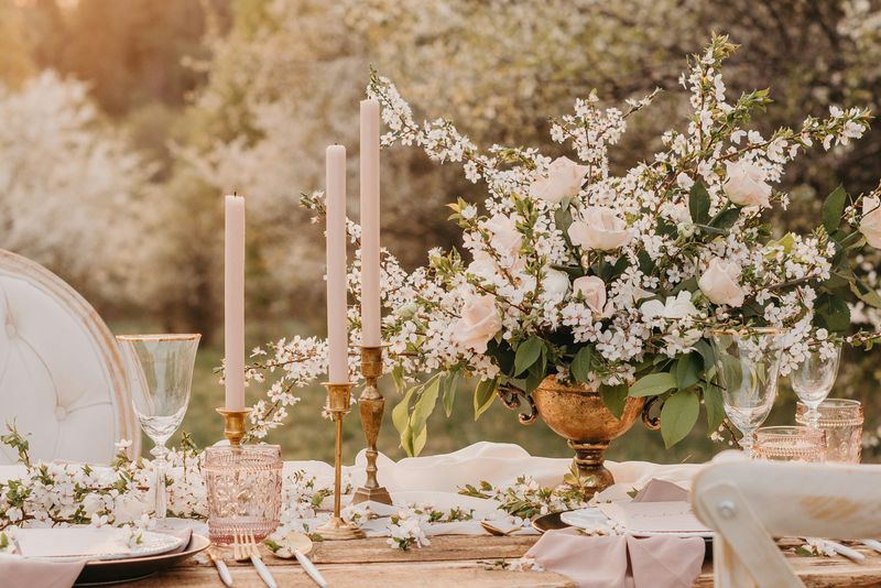 A table set with pale candles and blossom branches in an orchard at golden hour