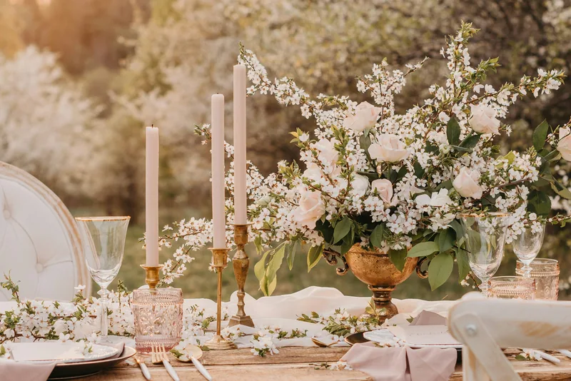 A table set with pale candles and blossom branches in an orchard at golden hour