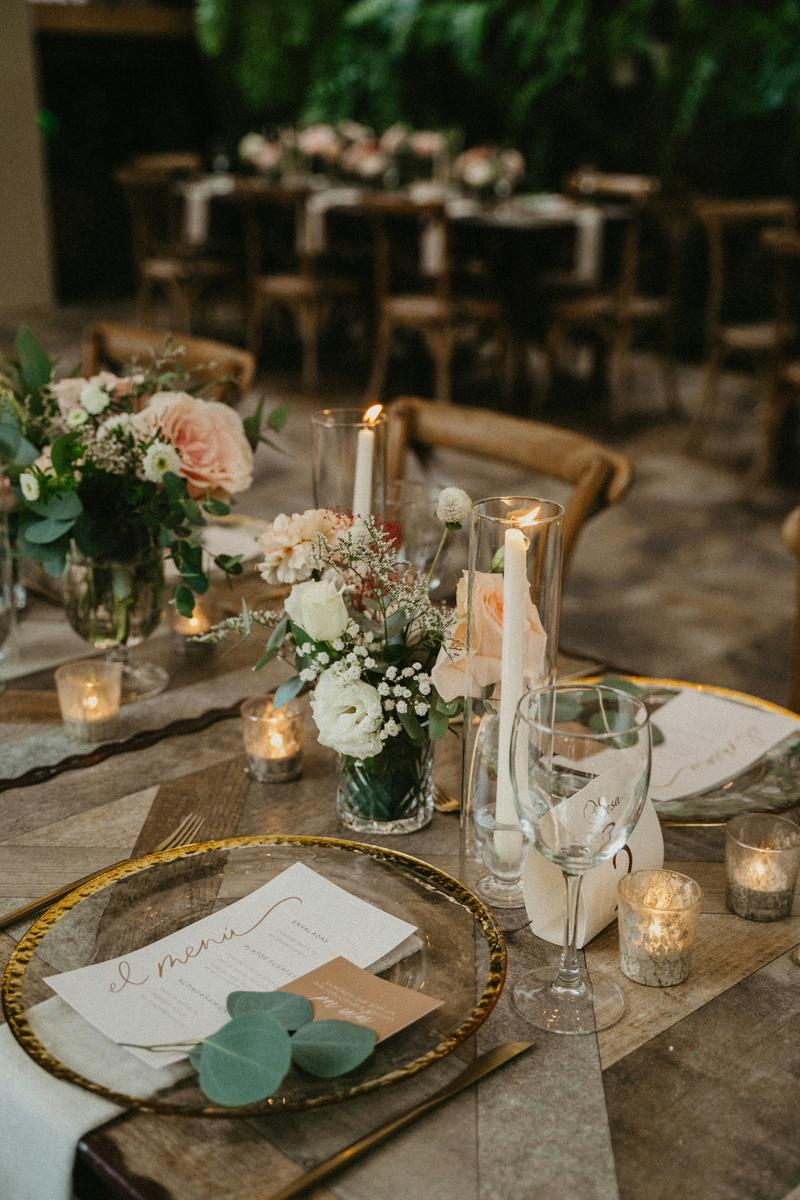 A place setting with a gold-rimmed charger, printed menu and candlelight on a wooden table