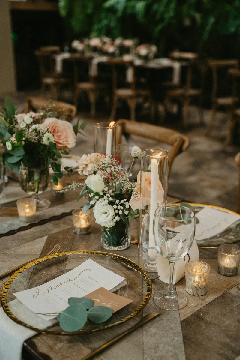 A place setting with a gold-rimmed charger, printed menu and candlelight on a wooden table