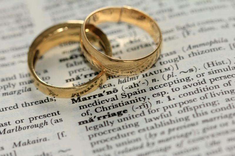 Two gold wedding bands resting on a dictionary page open to the word marriage